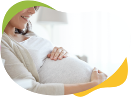 Těhotná žena, kterou netrápí nadýmání, sedí a směje se a přitom si hladí těhotenské břicho.